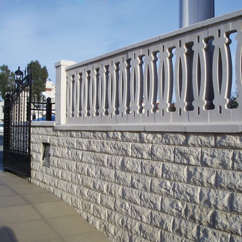 Barandilla de diseño con balaustres sobre un muro de piedra en la entrada de una propiedad.