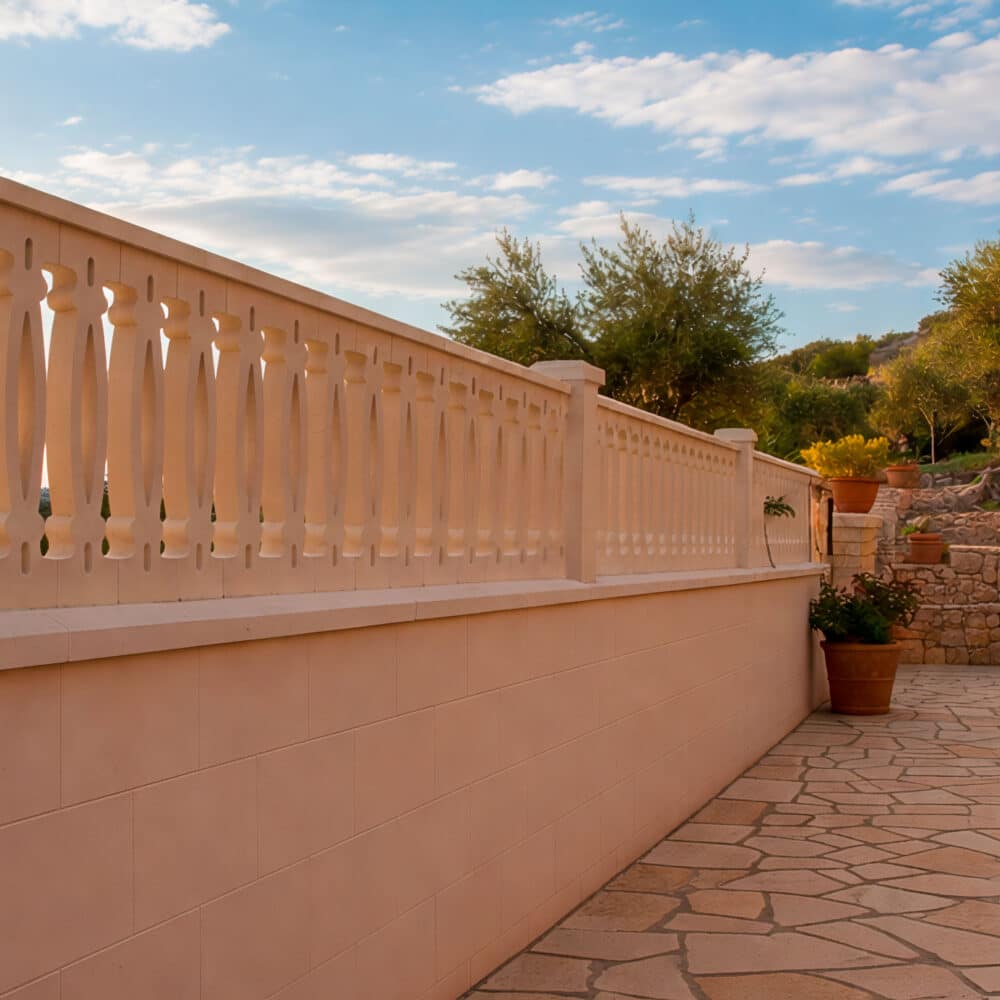 Larga balaustrada exterior de hormigón claro con diseño de corazón en un patio.