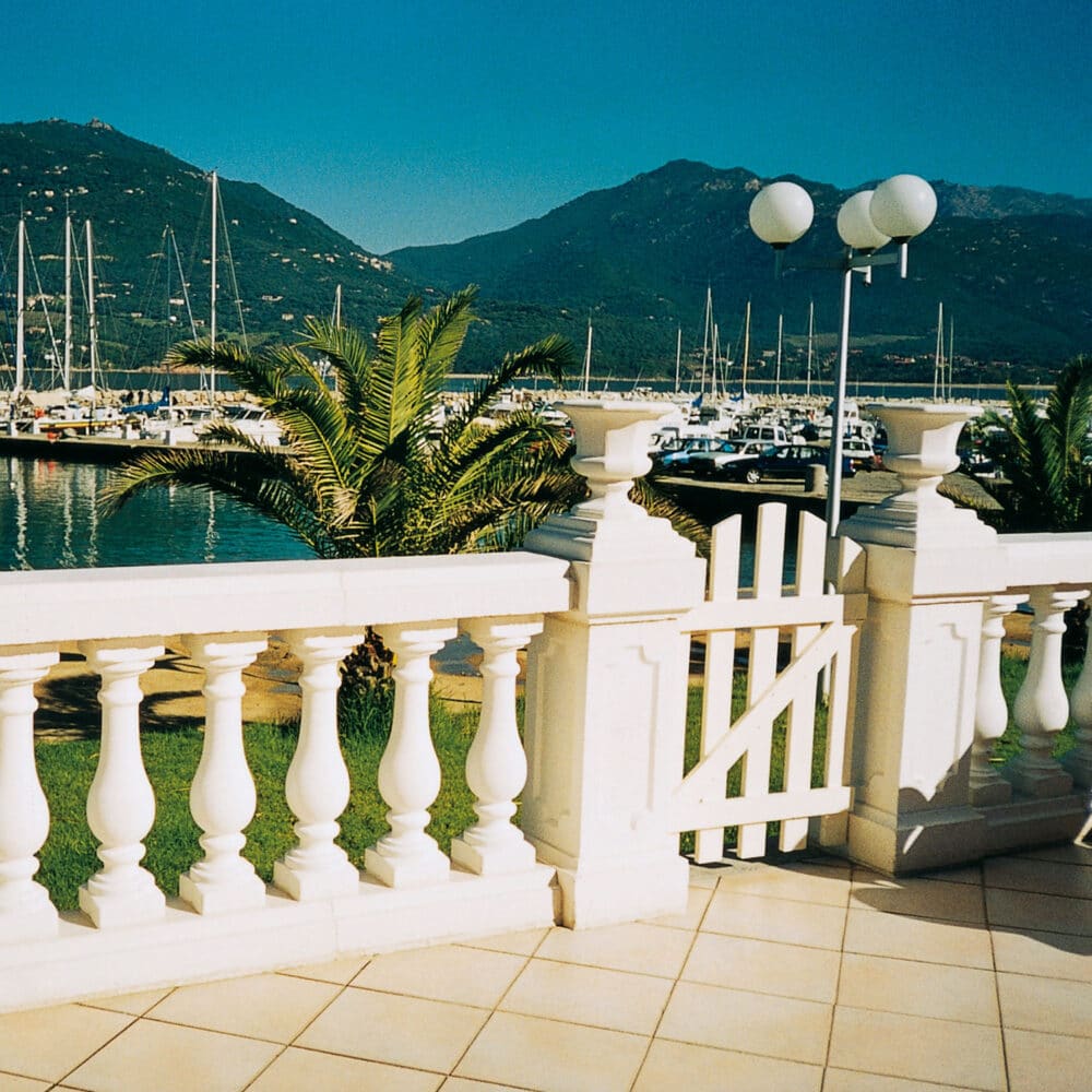 Balaustrada blanca con puerta frente a puerto y montañas al fondo