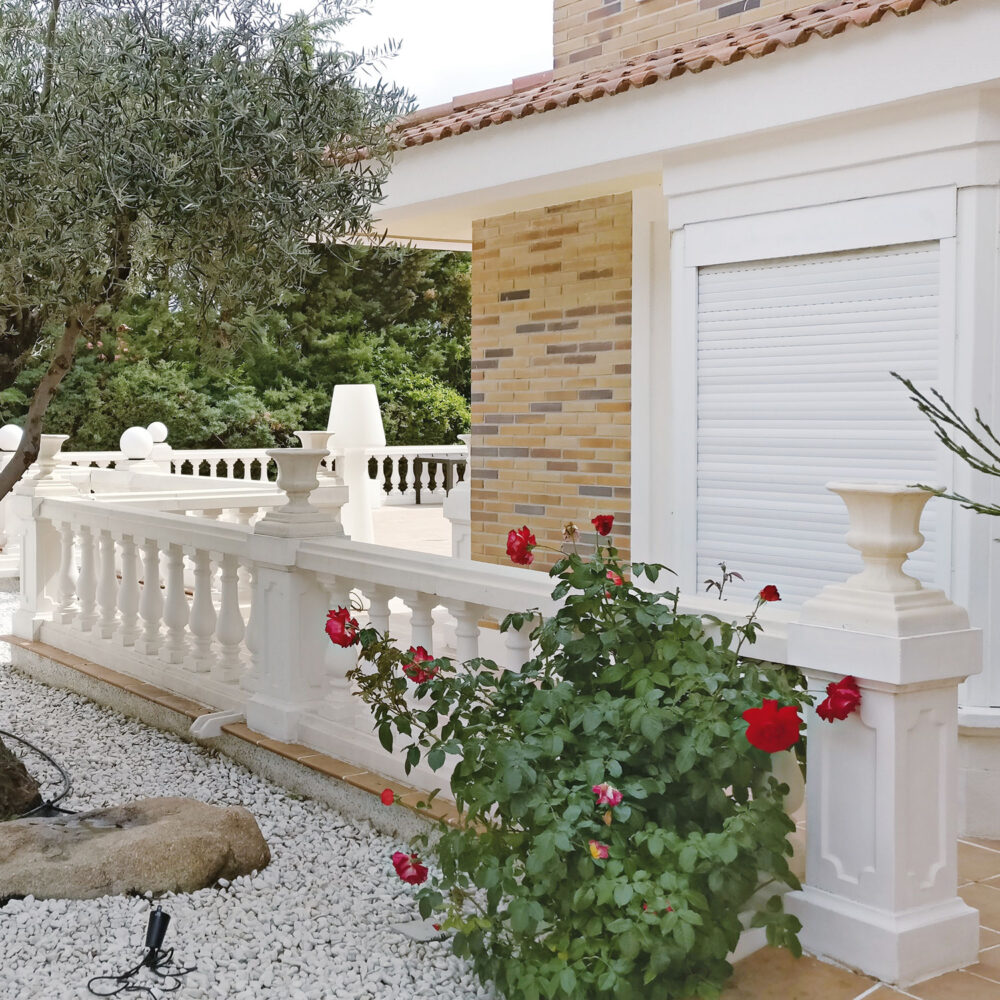 Jardín con balaustrada blanca de hormigón, rosales y detalles arquitectónicos clásicos